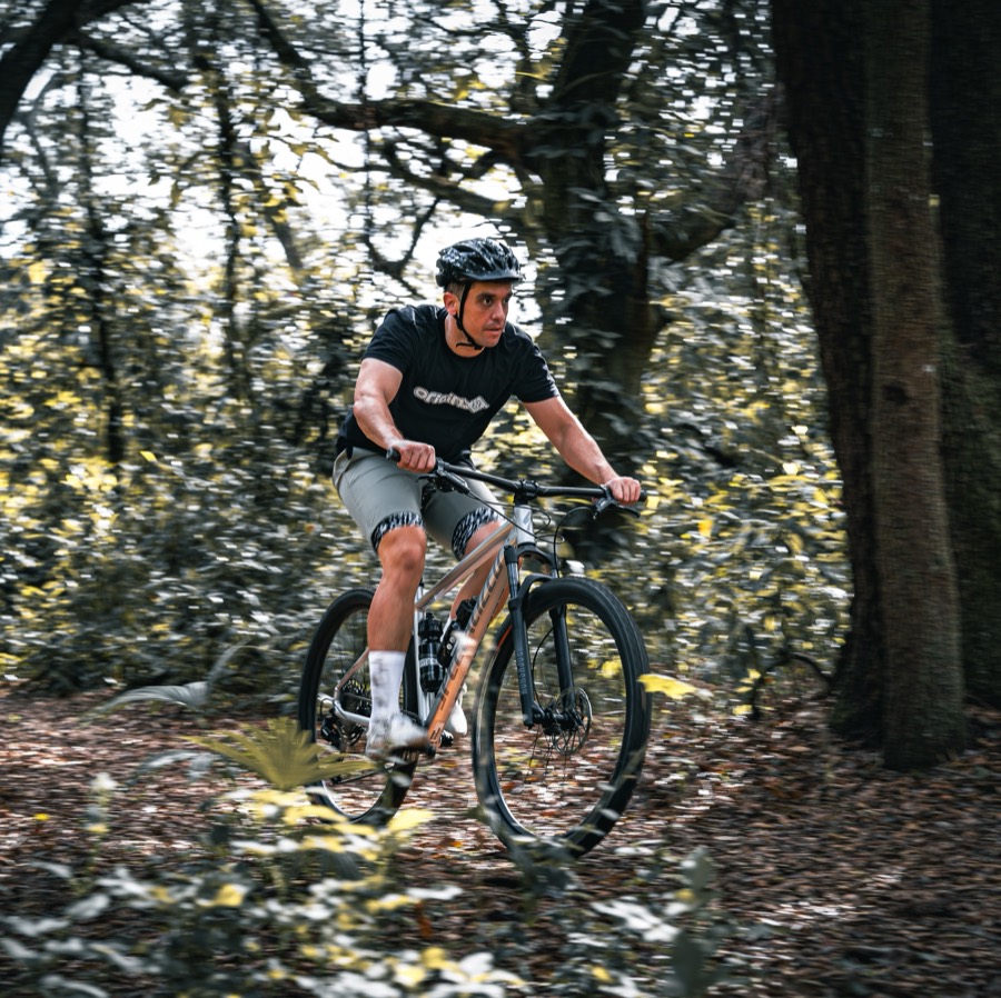 A rider in an Origin8 jersey riding a hardtail through wooded singletrack.